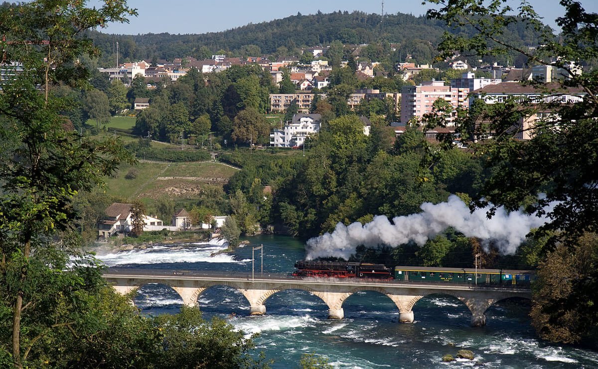 Photo of a train passing over a bridge upstream from the Rhine Falls Bridge with railway tracks