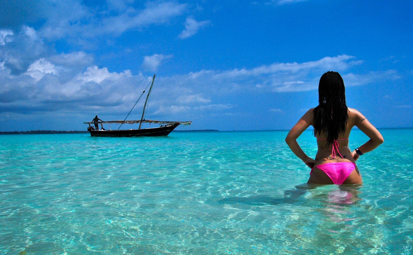 The girl stands in the ocean and looks at the boat standing further away Holidays in Zanzibar