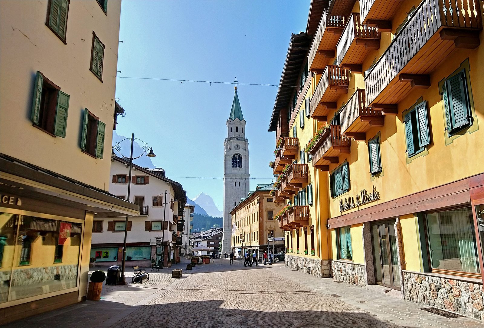 Pedestrian Corso Italia in Cortina d'Ampezzo with colourful buildings and the basilica bell tower