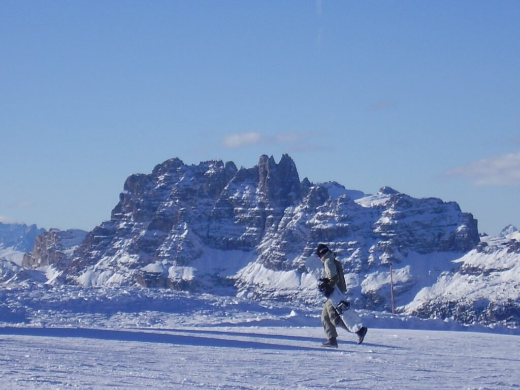 Snowboarder on a sunny piste on Monte Faloria in front of the jagged Croda da Lago peaks