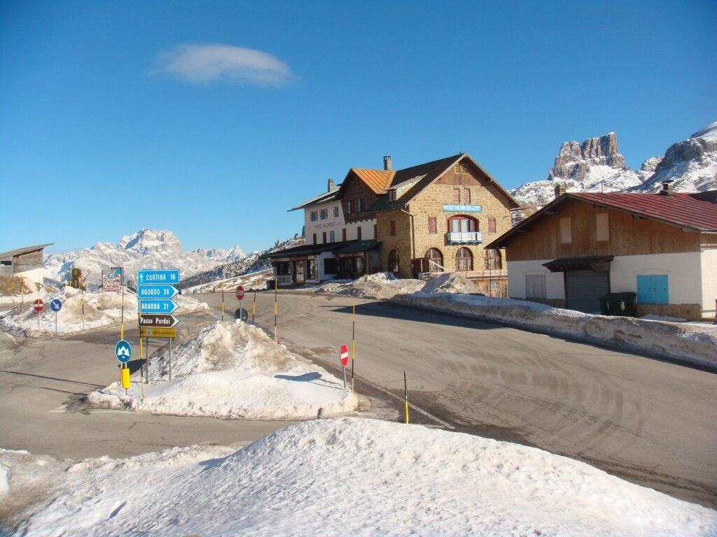 Snow-banked road and mountain hotel at Passo Falzarego in winter, with signposts towards Cortina d'Ampezzo