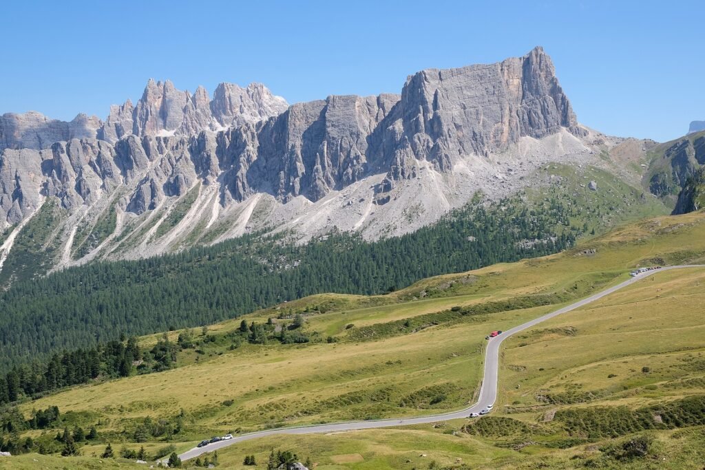 The SP638 road winding through green meadows below jagged Dolomite peaks on the way to Passo Giau
