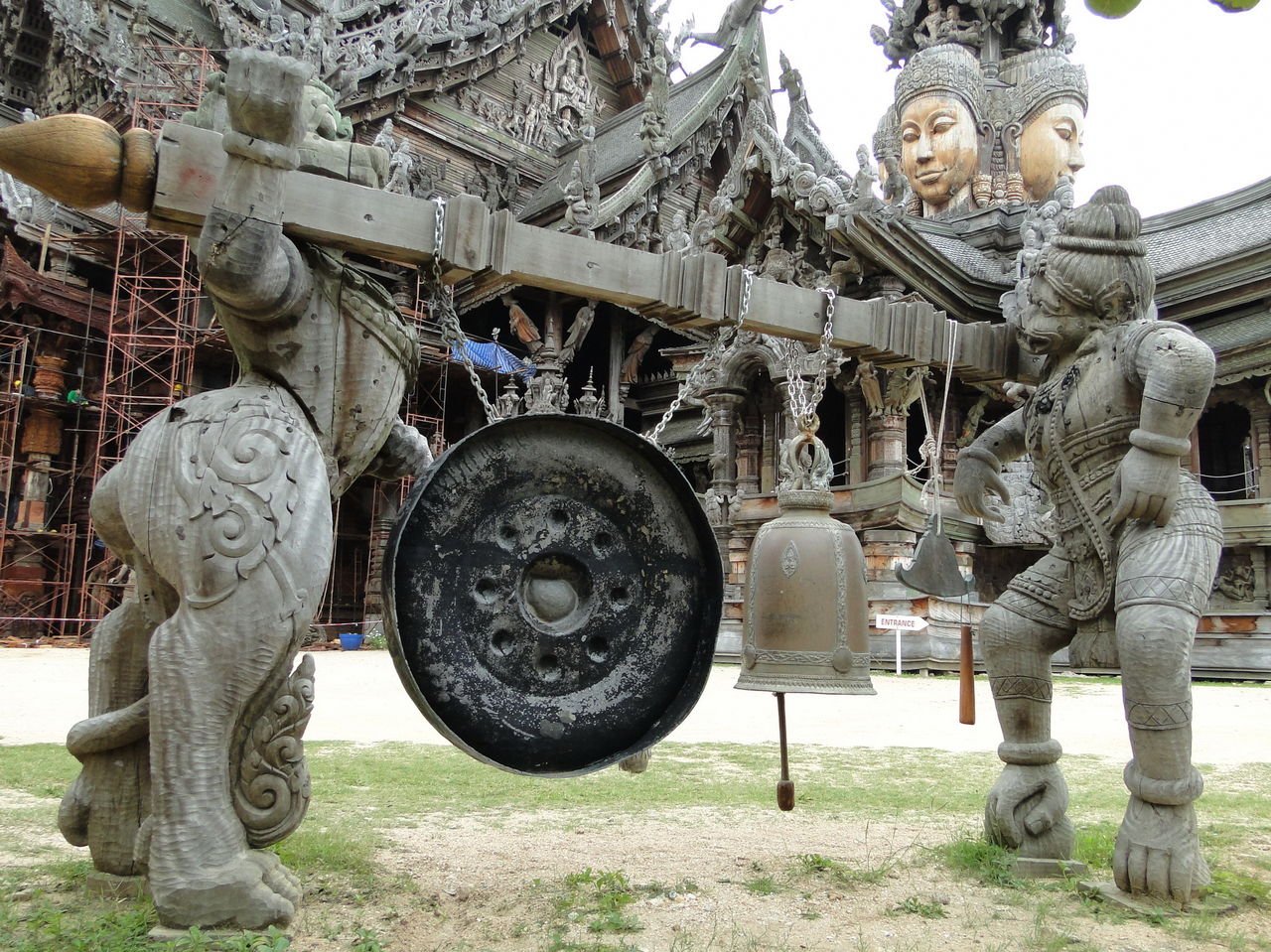 On the shoulders of two figures is a crossbar with three objects tied to it Gongs that purify karma